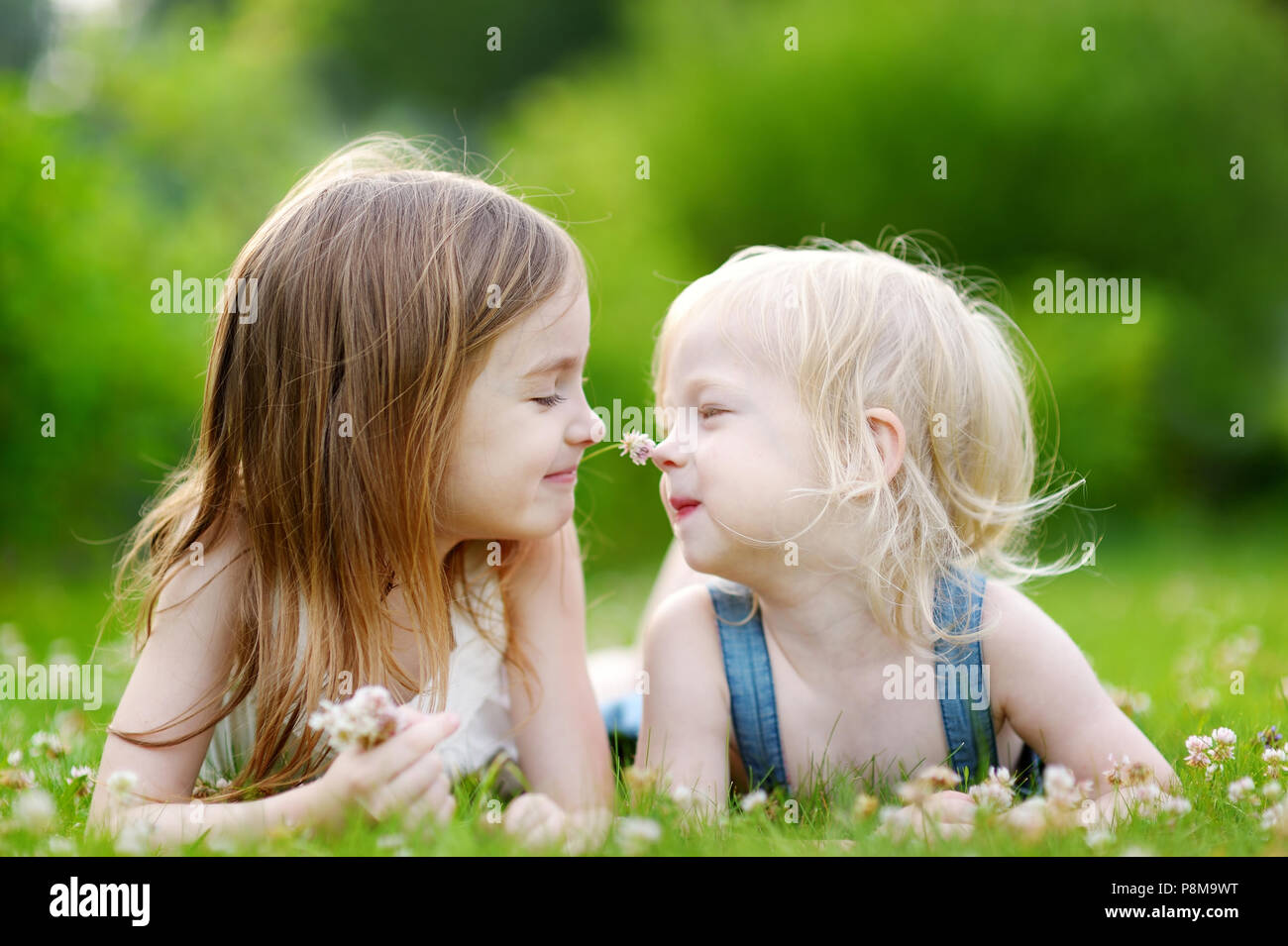 Two cute little sisters having fun while laying in the grass on a ...