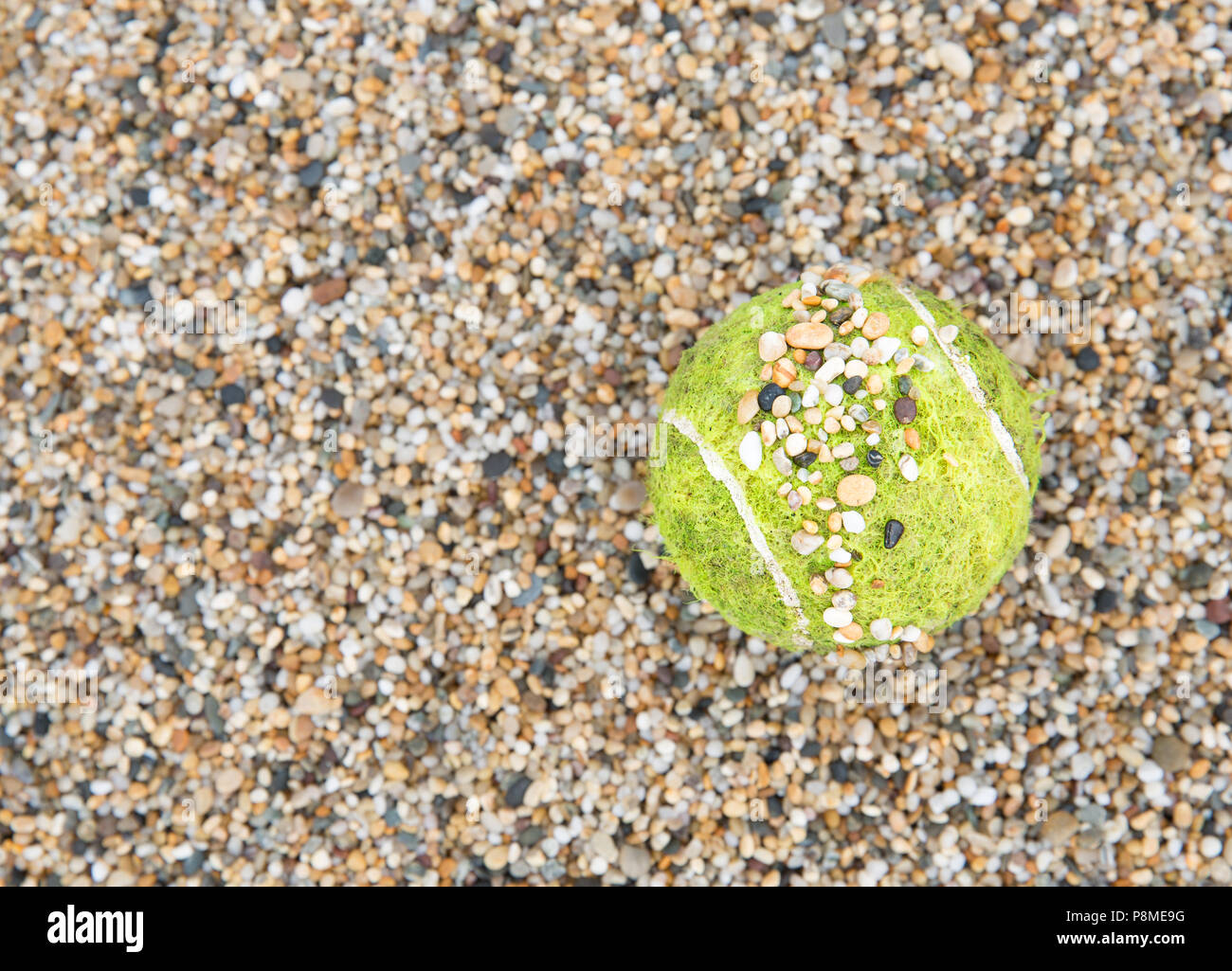 A tennis ball on a gravel court covered with small stones and pebbles with copy space in a sports background Stock Photo