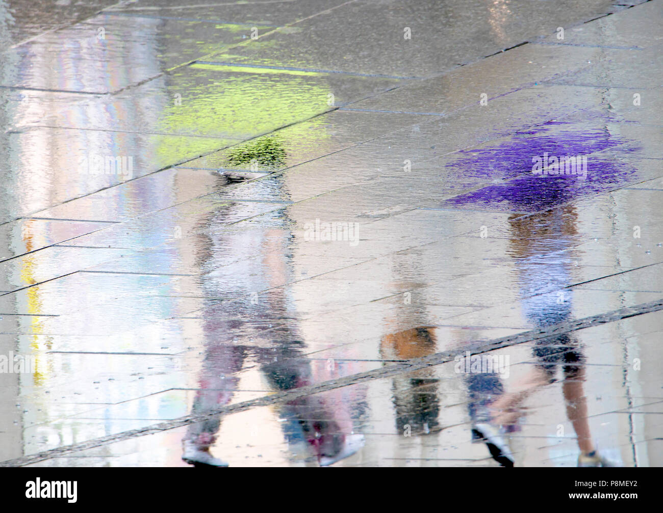 Blurry reflection shadow silhouettes of people walking under umbrellas on a rainy patterned city sidewalk on a spring day Stock Photo