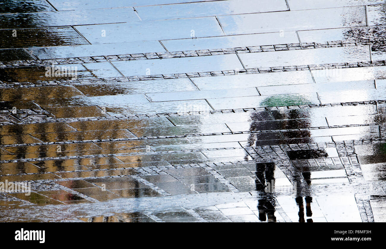 Blurry reflection shadow silhouettes of people walking on a rainy patterned city sidewalk on a spring day Stock Photo