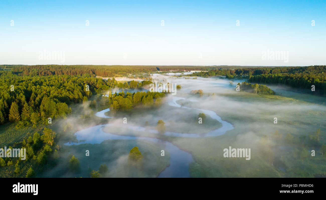 Foggy summer morning. Aerial landscape. River on green meadow frome above. Stock Photo