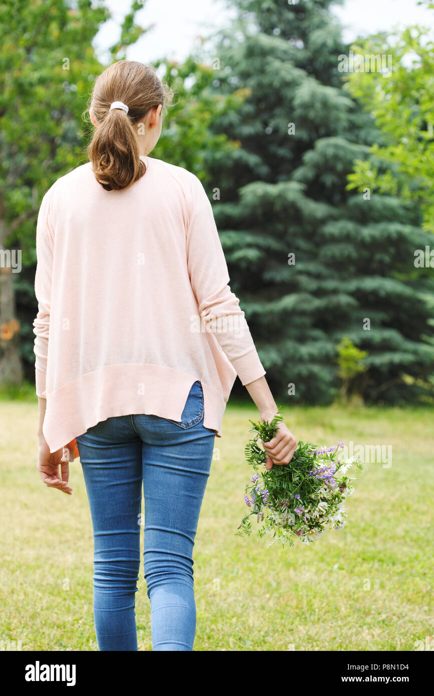 A young girl wearing in pink shirt and blue jeans holding a bouquet of wildflowers in hands Stock Photo