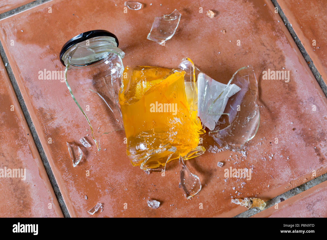 Broken marmalade glass jar on tile floor Stock Photo