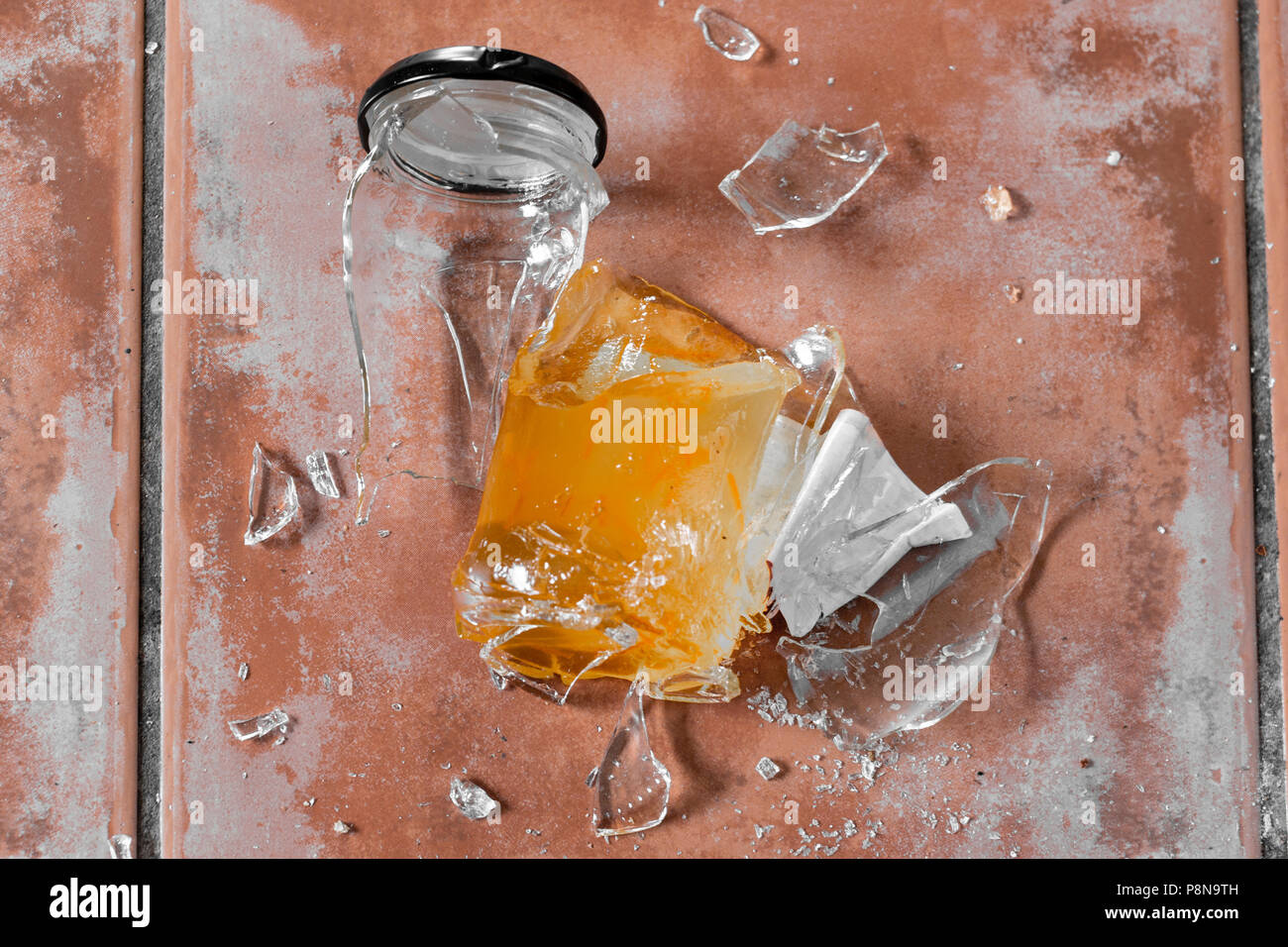 Broken marmalade glass jar on tile floor Stock Photo