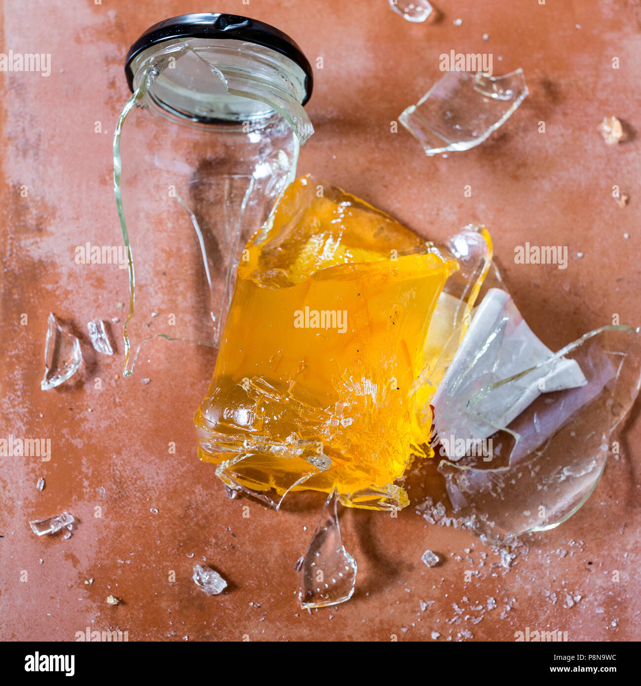 Broken marmalade glass jar on tile floor Stock Photo