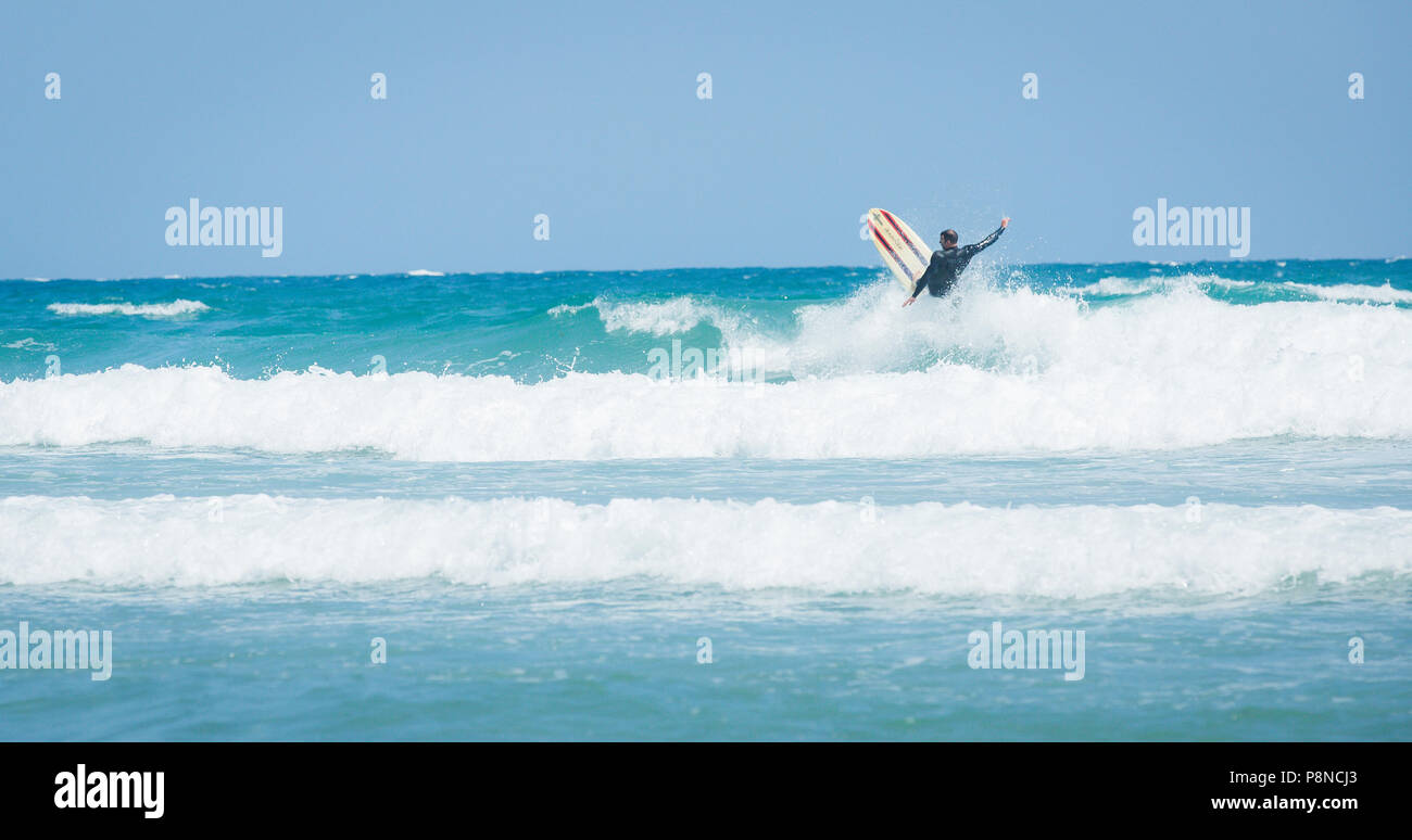 A surfer off the coast of Cornwall riding white waves on his surfboard before a wipeout. Stock Photo