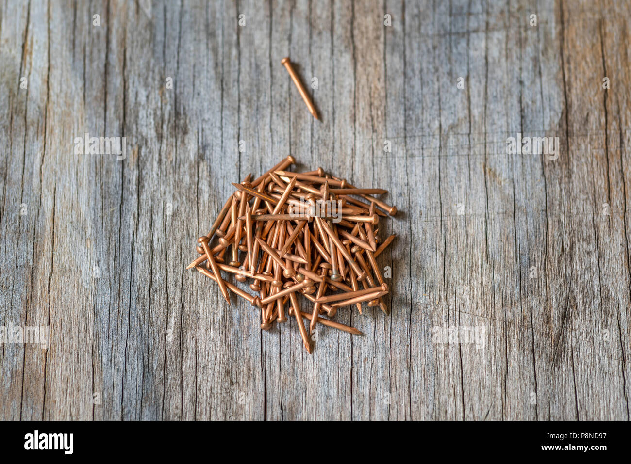 Close up of a group of bronze nails on a wood grain background. Stock Photo