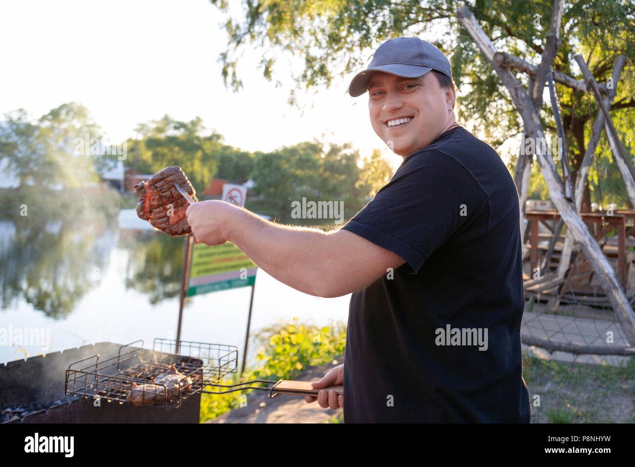 Barbecue party near lake or river outdoors. Man grilling meat beef