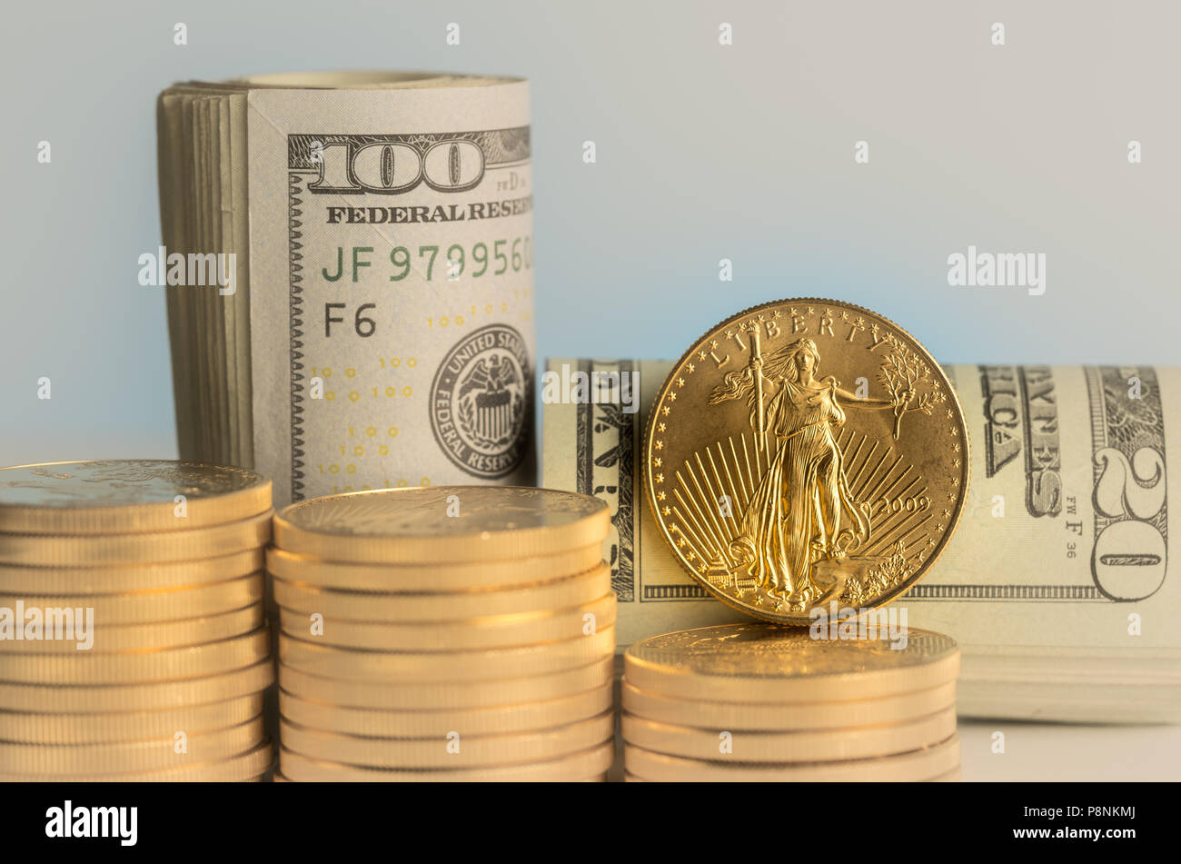 Pure gold coins in front of bank rolls of US currency Stock Photo