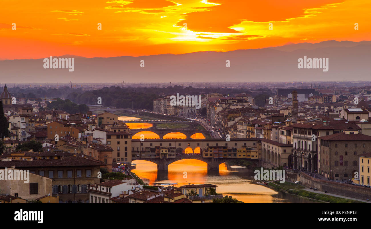 The setting sun shines it's last light on the Ponte Vecchio bridge and reflects off the Fiume Arno. Stock Photo