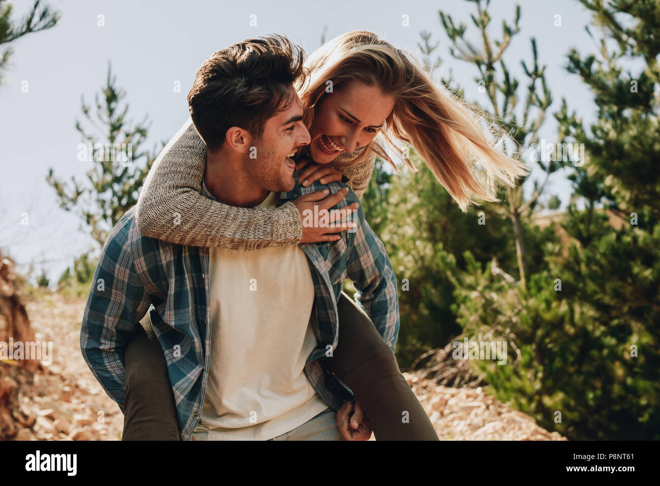 Man carrying girlfriend on his back while walking on a mountain trail. Couple enjoying themselves on a mountain trail. Stock Photo