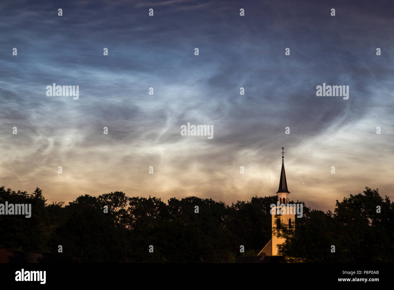 Noctilucent clouds over a church tower with the clock at three a.m. Stock Photo