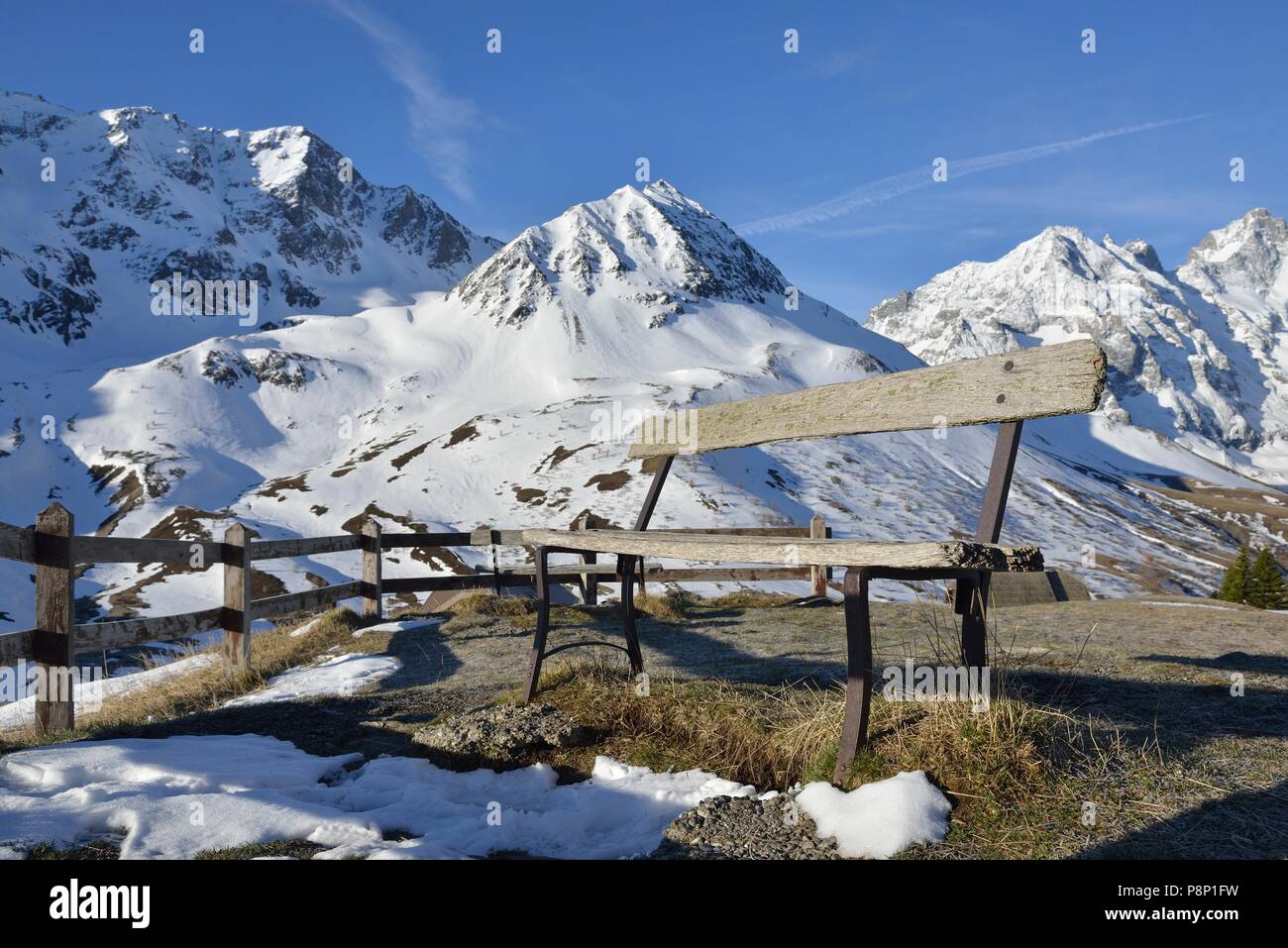 Lonely bench in front of snow covered alpine meadows at the end of the winter at the Col de Lautaret Stock Photo