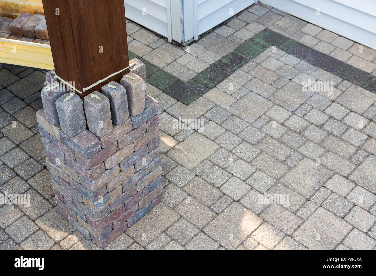 Building a brick pillar around a timber gazebo leg gluing the grey bricks into position in a DIY concept on an exterior paved patio Stock Photo