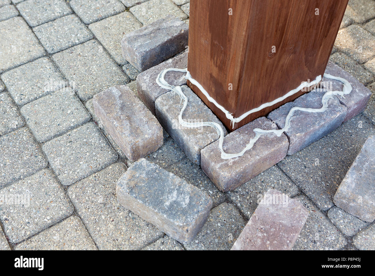 Glue applied to grey bricks around a wooden pillar during installation of a new gazebo on the patio Stock Photo