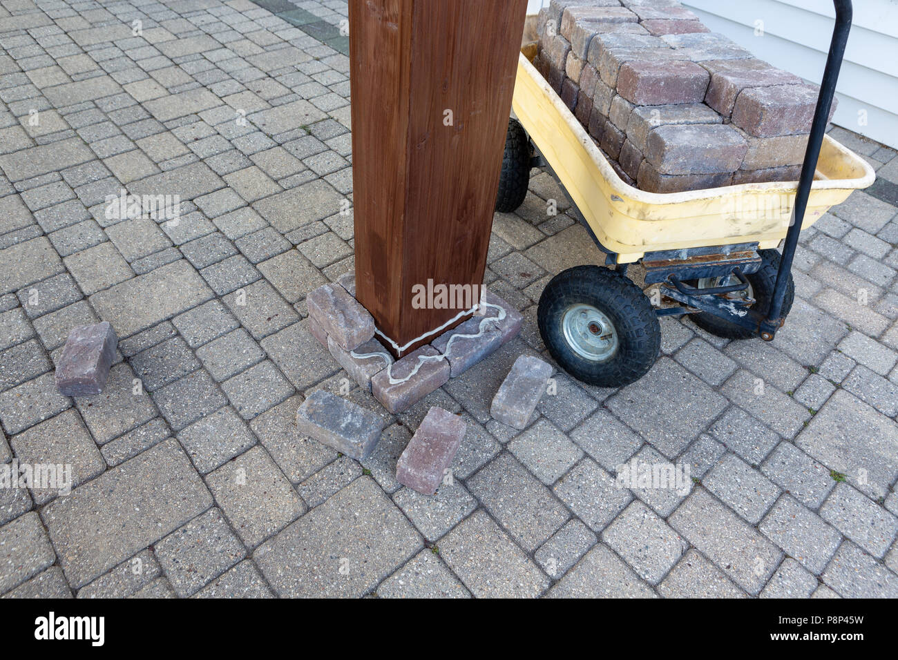 Diy improvements to an exterior patio gluing paving bricks loaded in a wheelbarrow around the wooden leg of a newly installed gazebo or pergola Stock Photo