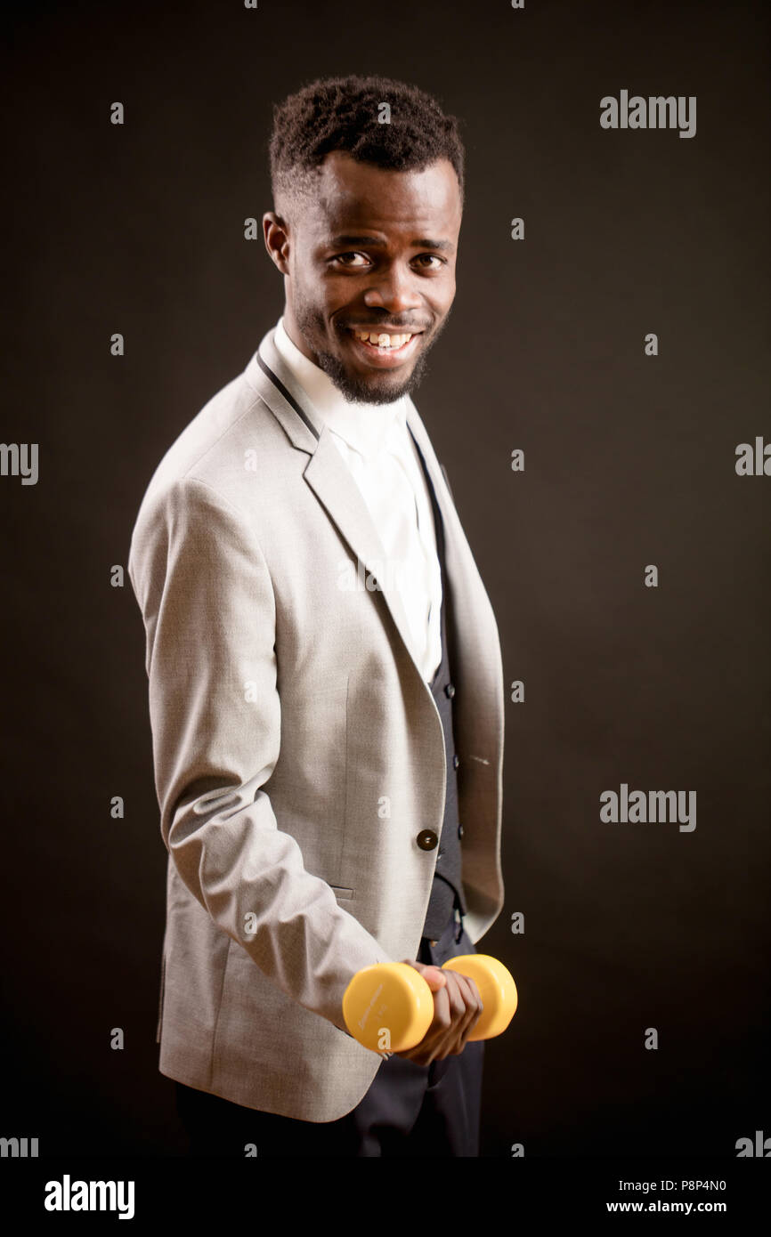 smiling Afro guy with yellow dumb-bell looking at the camera. lift weight. workout while working. like sport Stock Photo