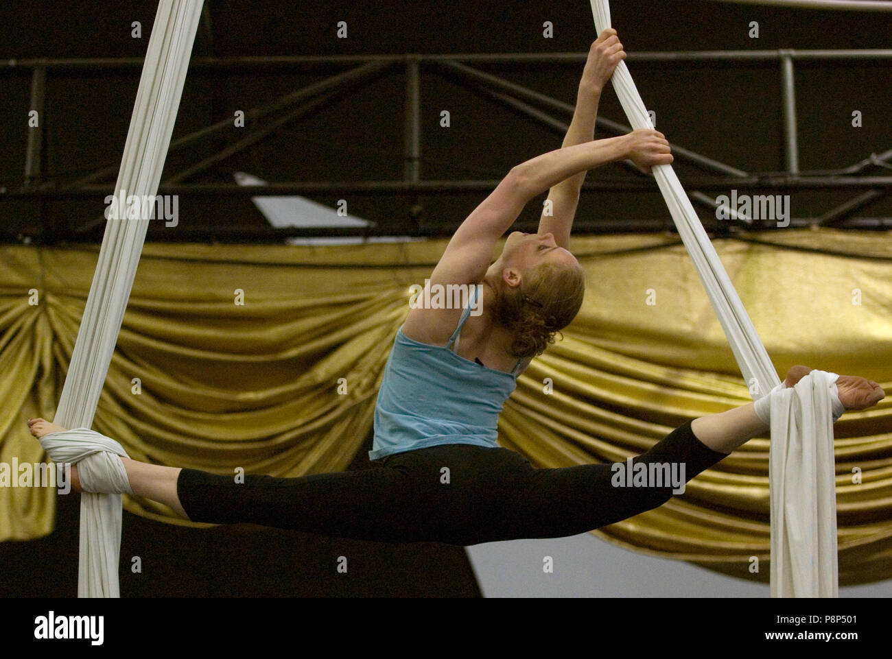 A female acrobat suspends herself in a splits position by wrapping ...