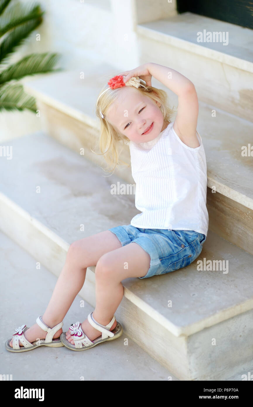 Adorable little girl sitting on stairs on warm and sunny summer day in typical italian town Stock Photo