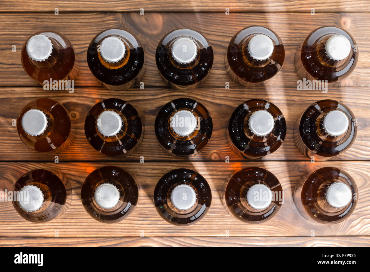 15 neatly aligned rows of bottled craft beer capped with bottle tops viewed top down on a wooden table Stock Photo