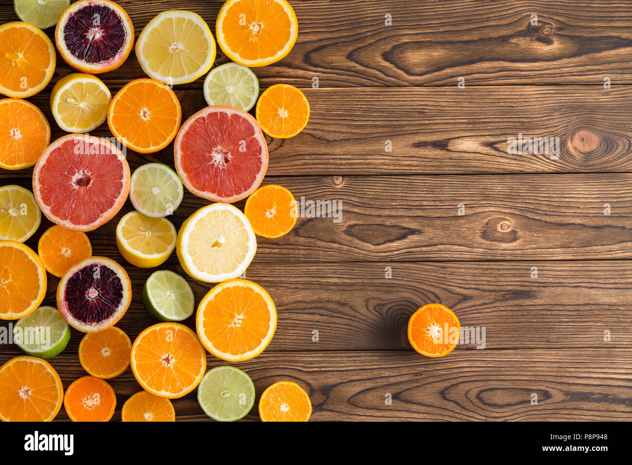 Assorted fresh cut citrus fruits on a wooden background with copy space and a single clementine set to the side viewed from above Stock Photo