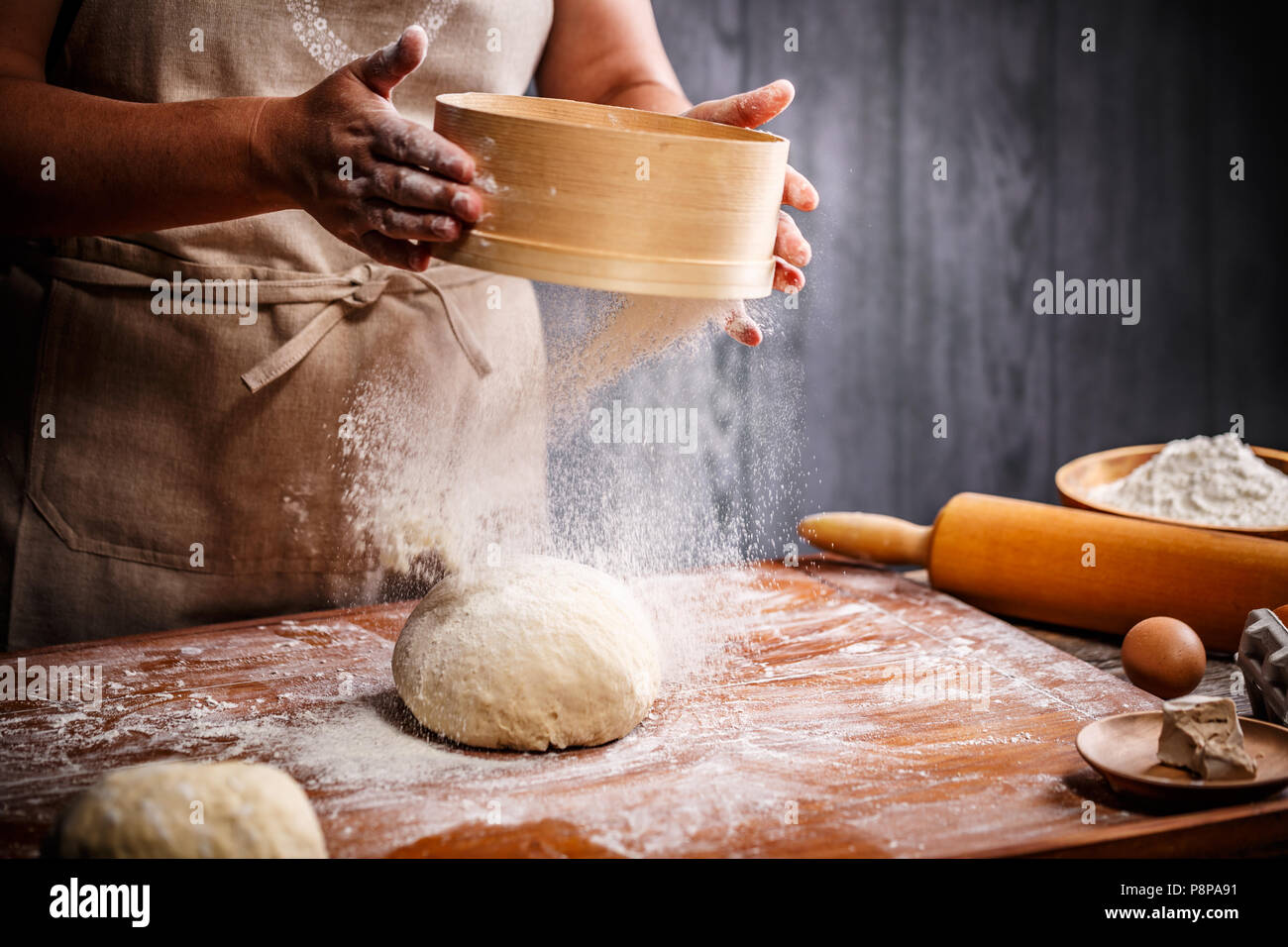 Woman hands sifting flour over dough Stock Photo