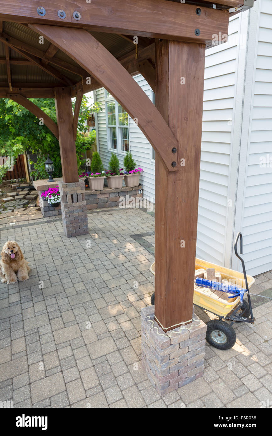 DIY home improvements adding a wooden gazebo on an exterior paved patio building a brick pillar around the wooden legs Stock Photo