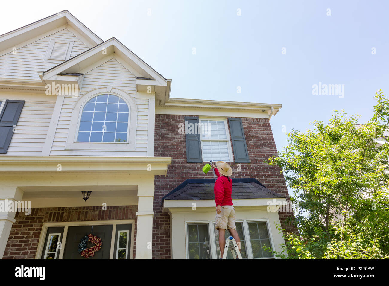 Man standing on a ladder cleaning the house trims with a power nozzle