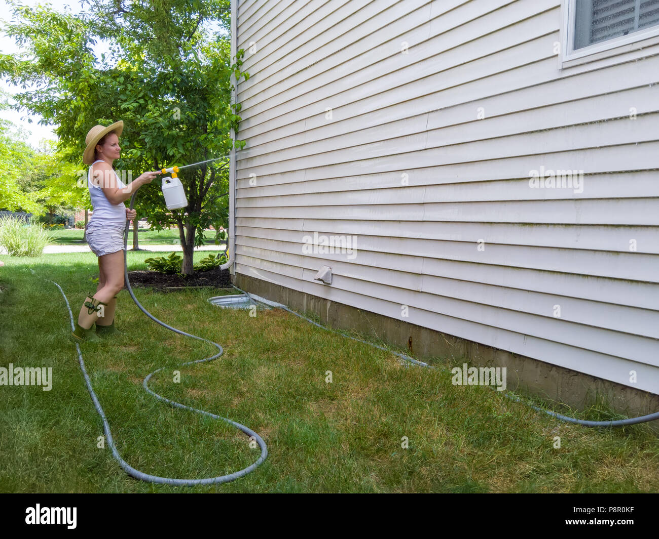 Attractive housewife spraying down the exterior facade of her home