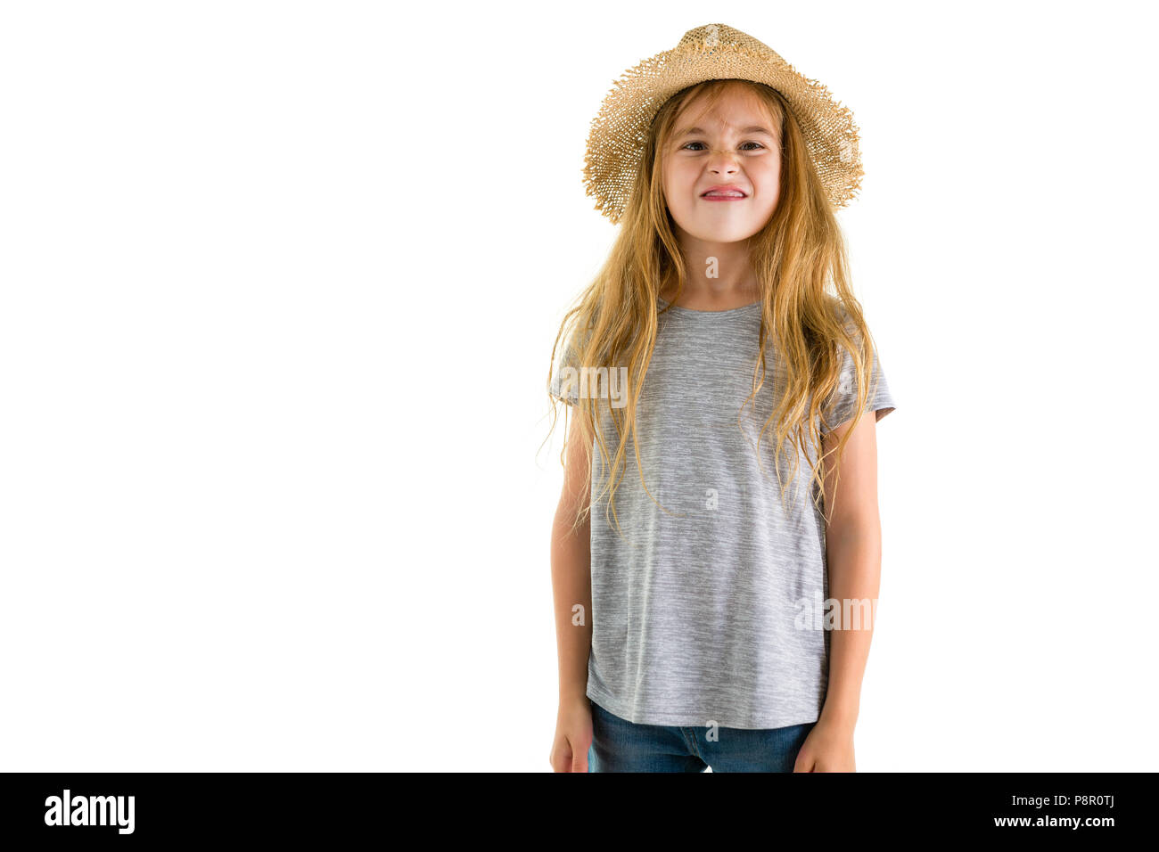 Playful little blond girl in a trendy straw sunhat sticking out her tongue at the camera with a smile isolated on white Stock Photo