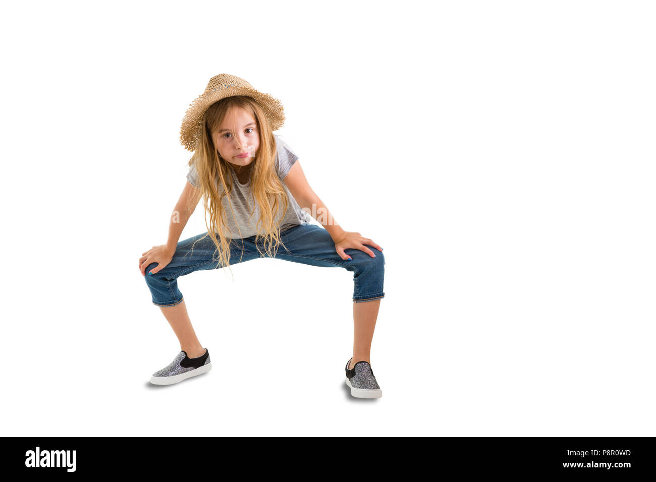 Cute thin young girl in a trendy straw hat and denim jeans crouching down looking at the camera isolated on white with copy space Stock Photo