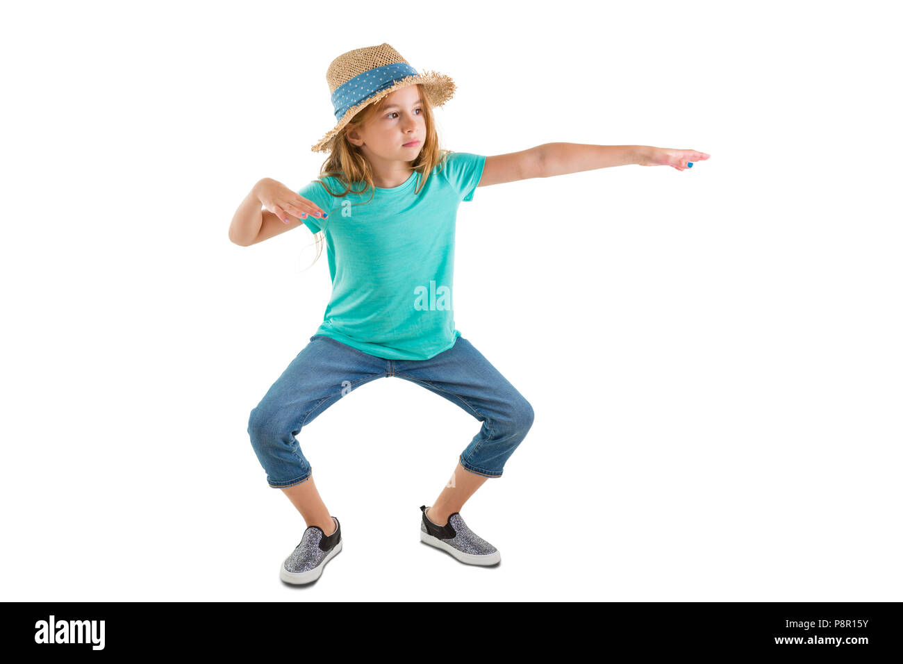 Young girl in casual denim jeans and a straw hat standing making funky dance moves bending at the knee with outstretched arms isolated on white Stock Photo