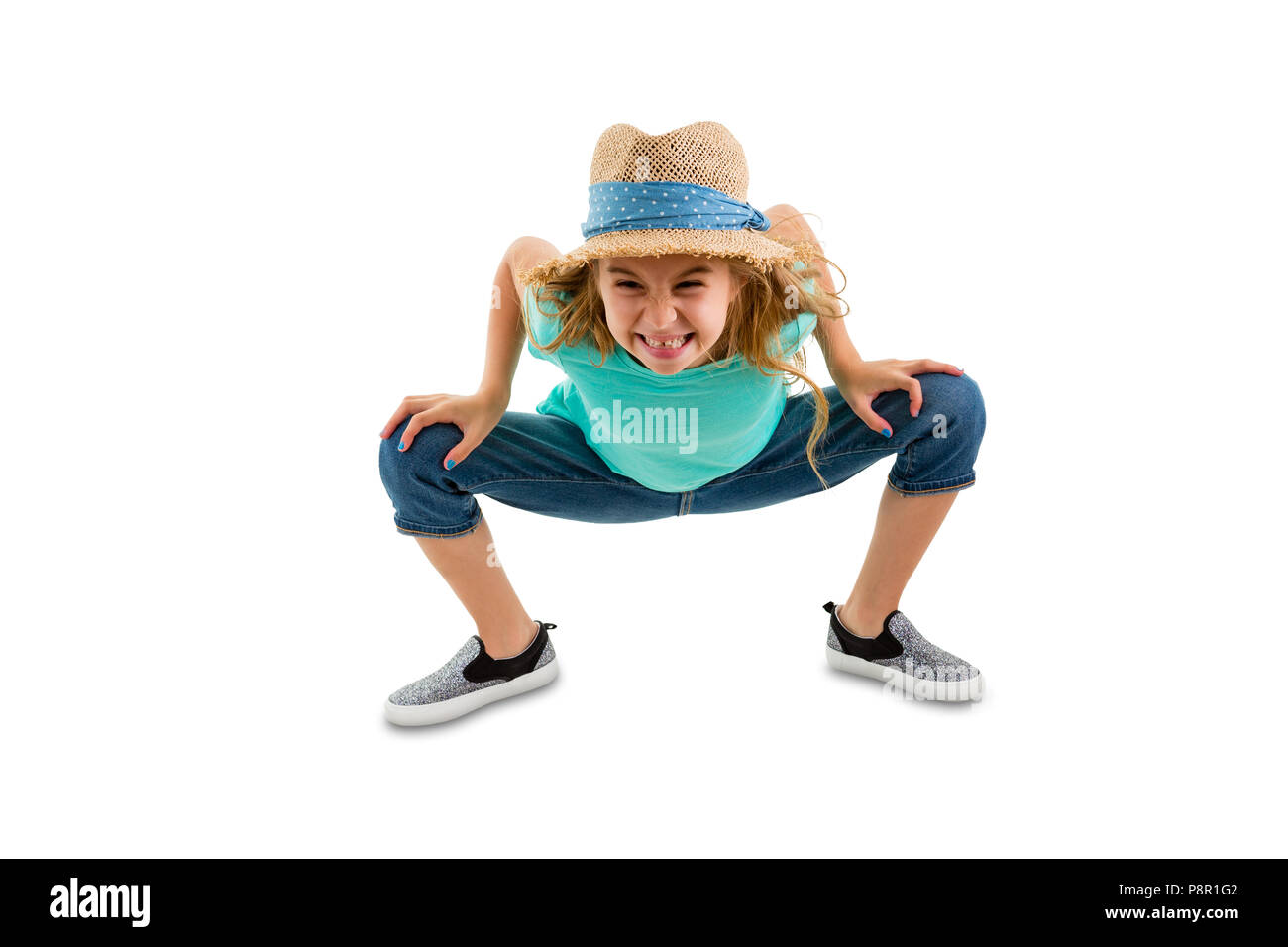 Mischievous naughty little girl bending forwards towards the camera with an impish grin in a trendy straw sunhat and jeans Stock Photo