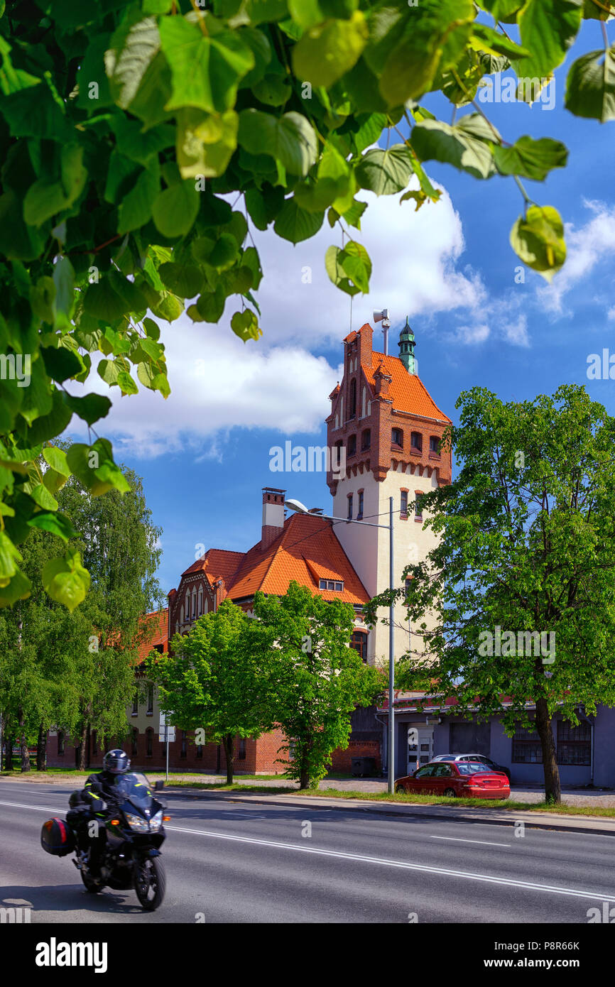 Firehouse building in Riga on a background of green trees and passing by on the street biker Stock Photo