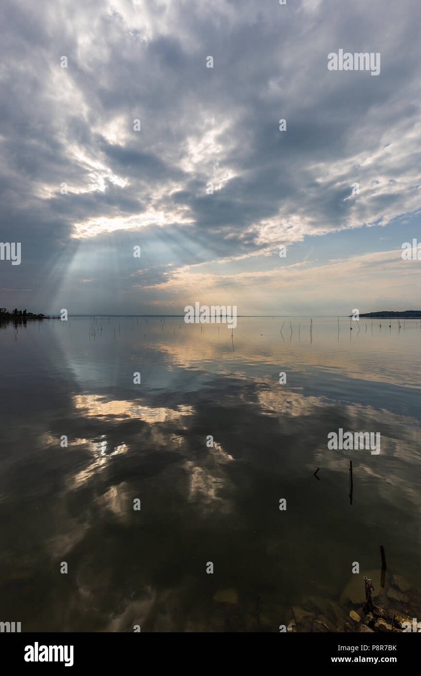 Perfectly symmetric and spectacular view of a lake, with clouds, sky and sun rays reflecting on water Stock Photo