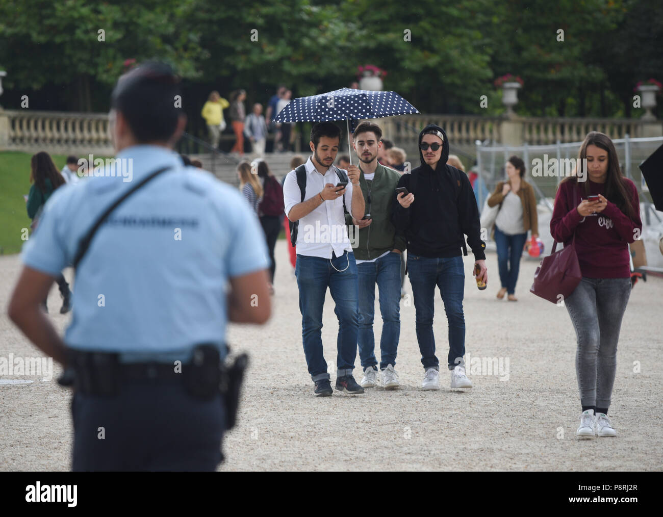 July 14, 2016 - Paris, France: Police look at youths taking part in a mass Pokemon hunt in the Luxembourg Garden in central Paris. Hundreds of players of the new Pokemon Go game showed up to take part in a massive hunt despite the authorities' attempt to cancel the event. Despite playing mostly solo, the Pokemon Go users enjoyed to interact and meet other players. Millions of users have already downloaded the game, which requires users to catch on-screen pokemon characters using their real-world location.  Des jeunes participent a une chasse au Pokemons dans le jardin du Luxembourg avec l'appl Stock Photo