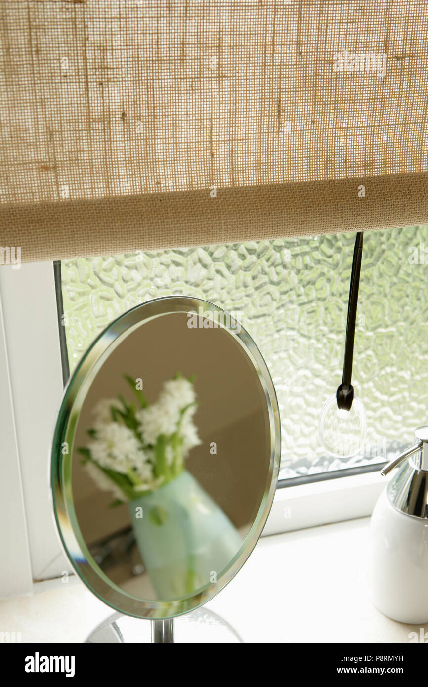 Close-up of linen blind on frosted glass window with small mirror on windowsill Stock Photo