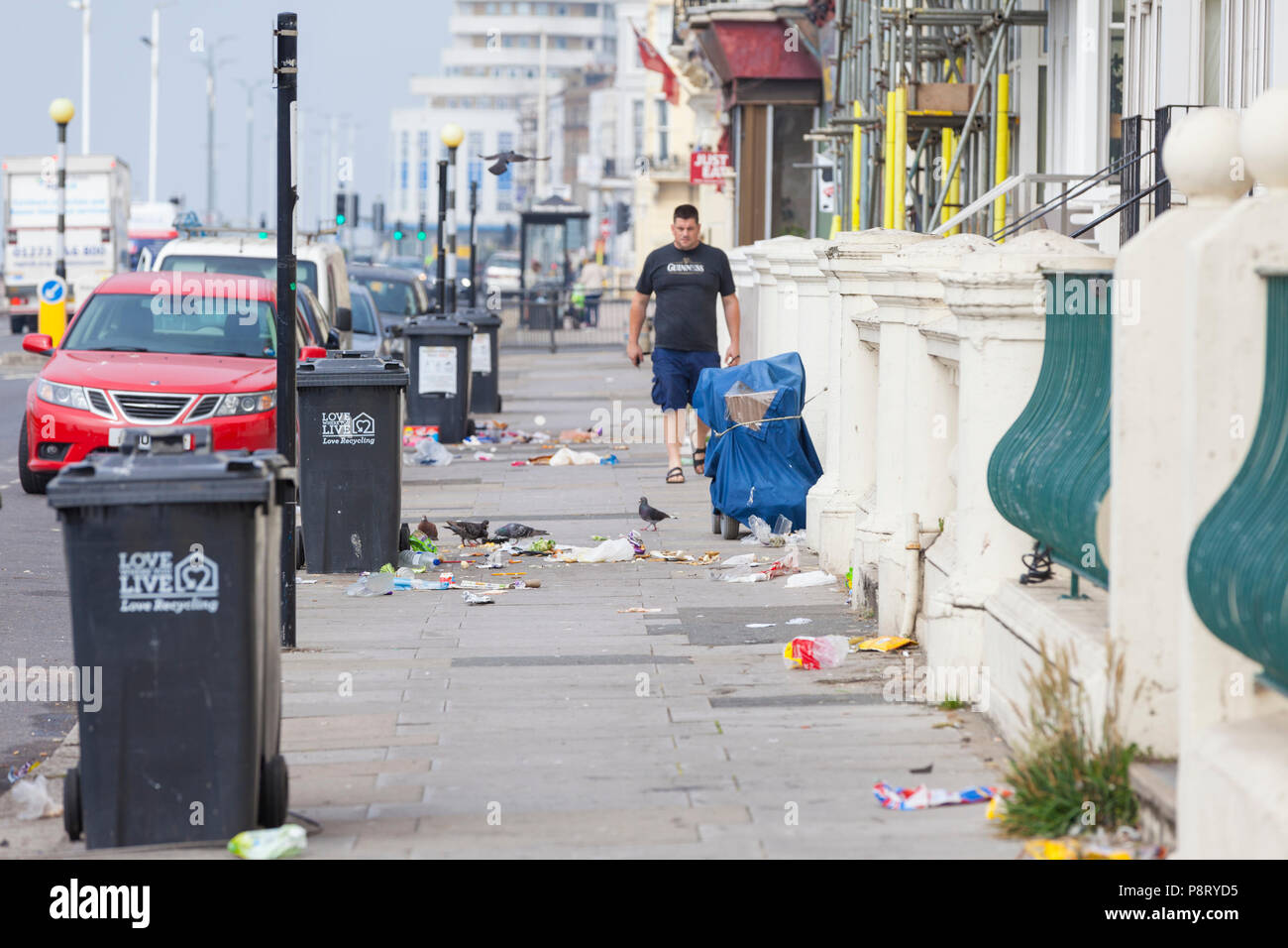 Person walking past a litter strewn street with pigeons picking at rubbish lying on the floor in hastings, east sussex, uk Stock Photo