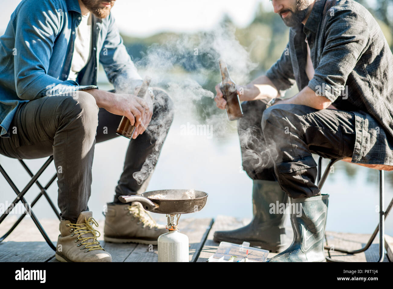 Two fishermen frying fish sitting with beer during the picnic on the
