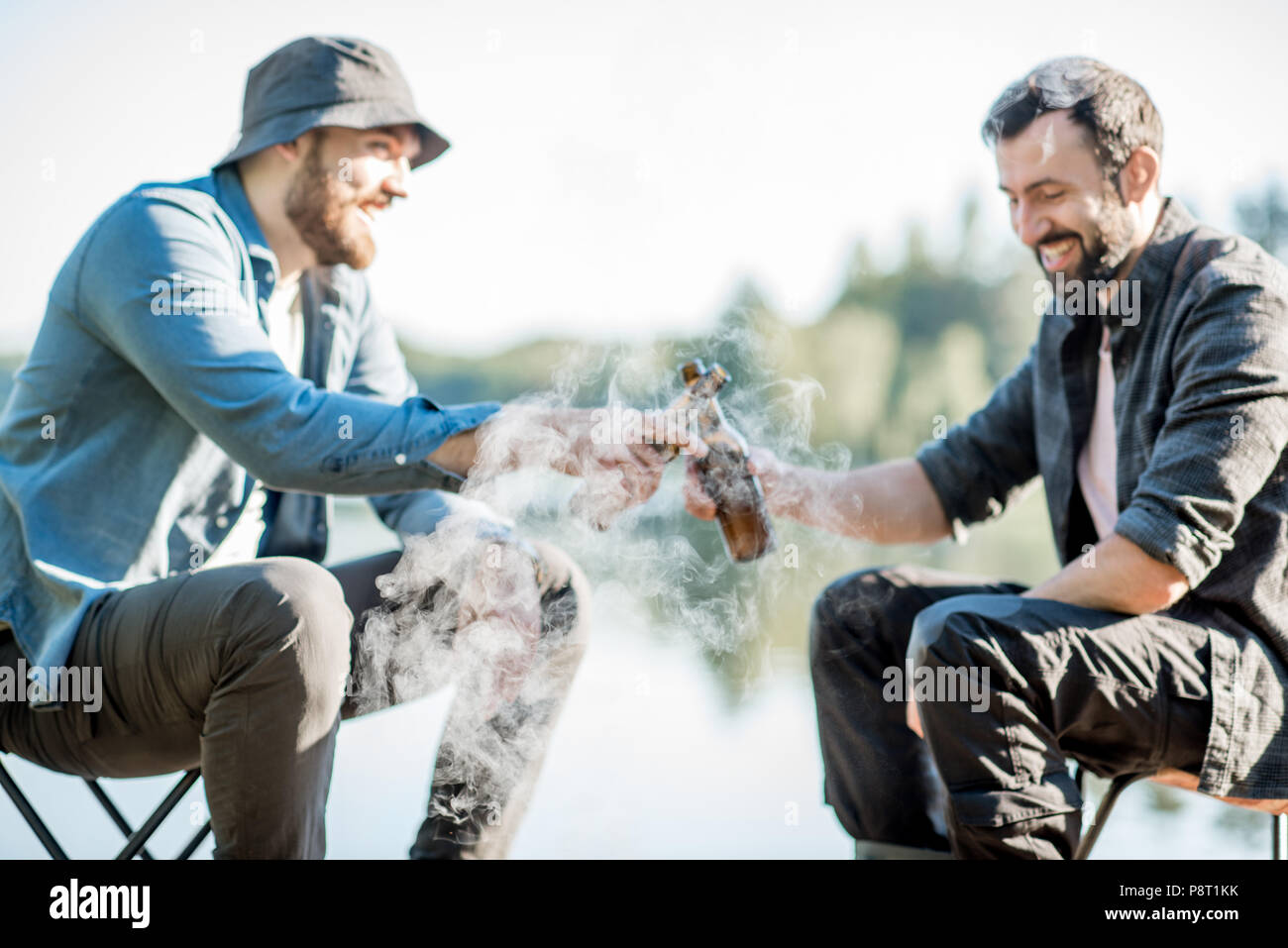 Two fishermen frying fish sitting with beer during the picnic on the