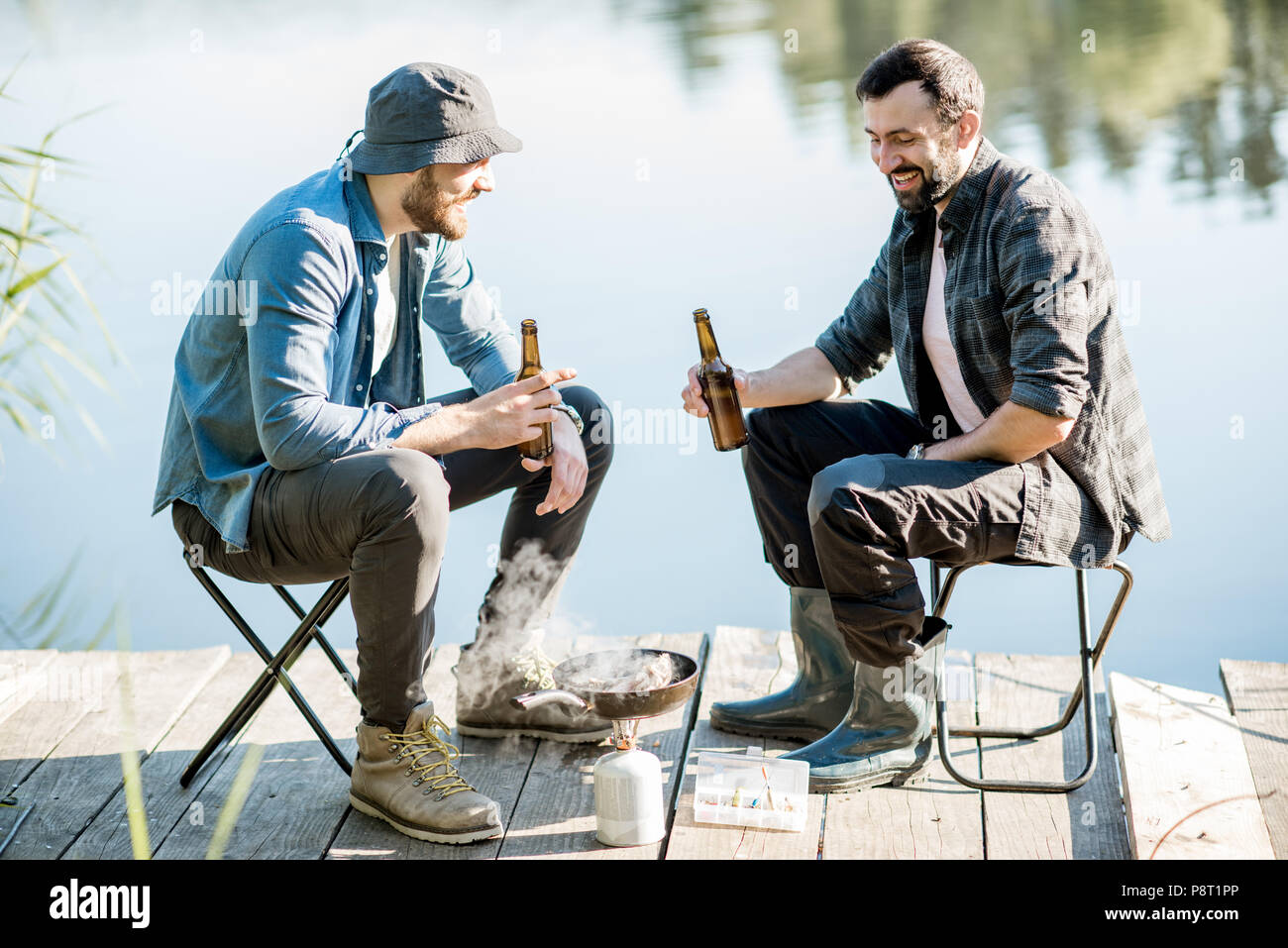 Two fishermen frying fish sitting with beer during the picnic on the
