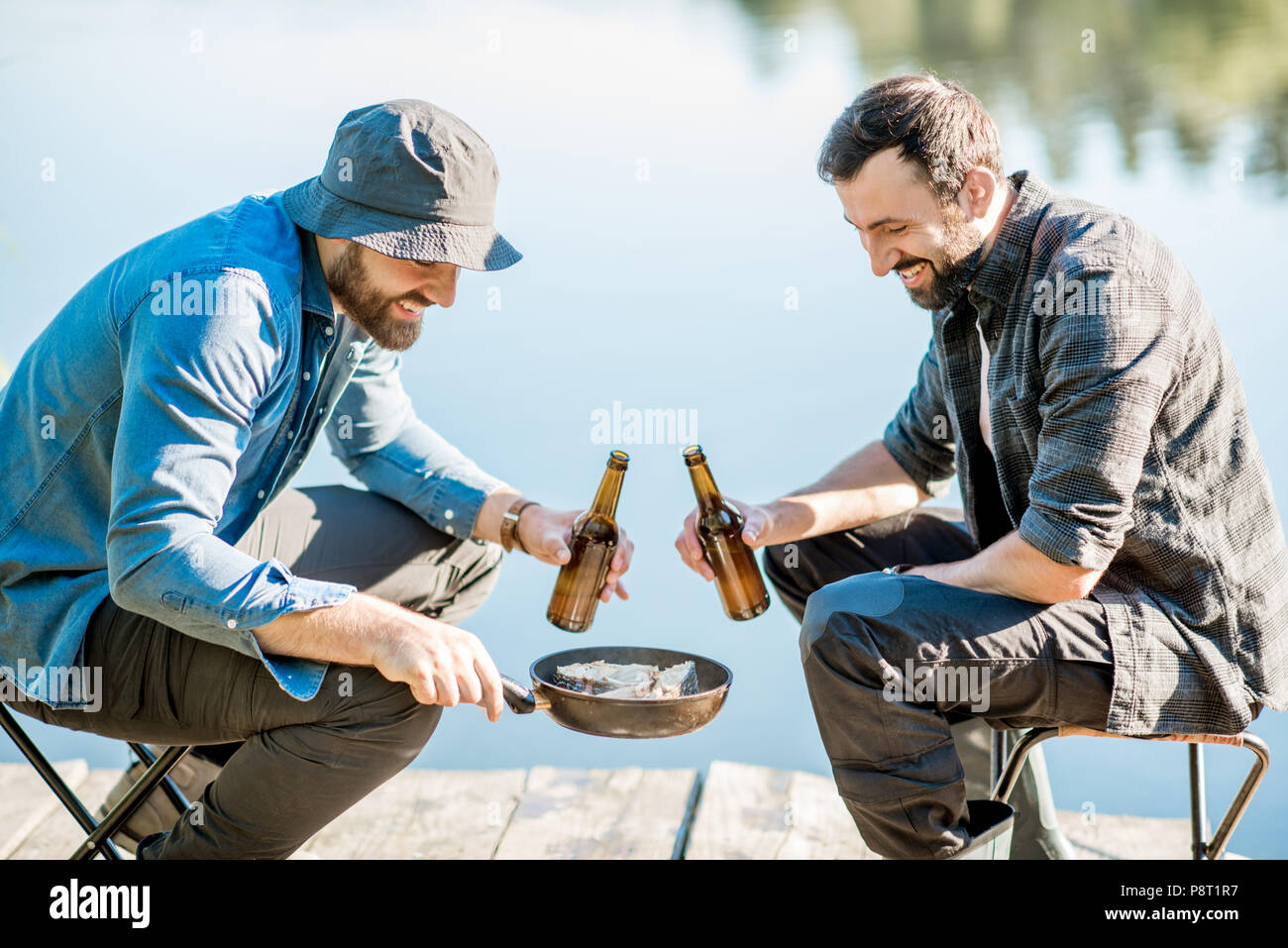 Two fishermen frying fish sitting with beer during the picnic on the