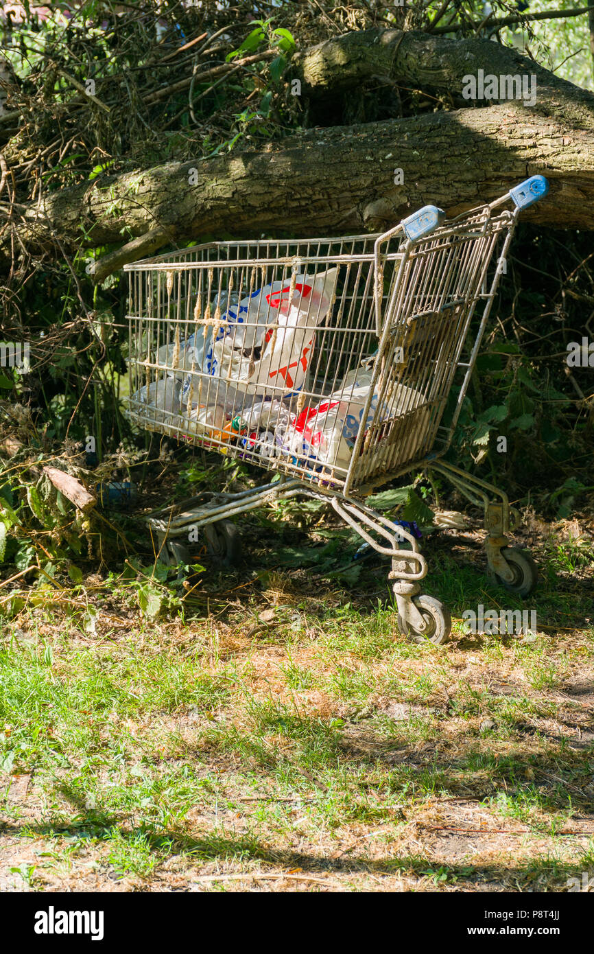 A discarded shopping trolley with plastic bags and rubbish in it