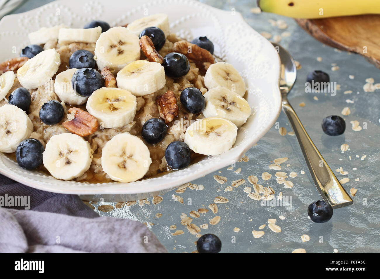 Hot breakfast of healthy oatmeal with pecans, bananas, blueberries and honey over a rustic background. Image shot from overhead. Stock Photo