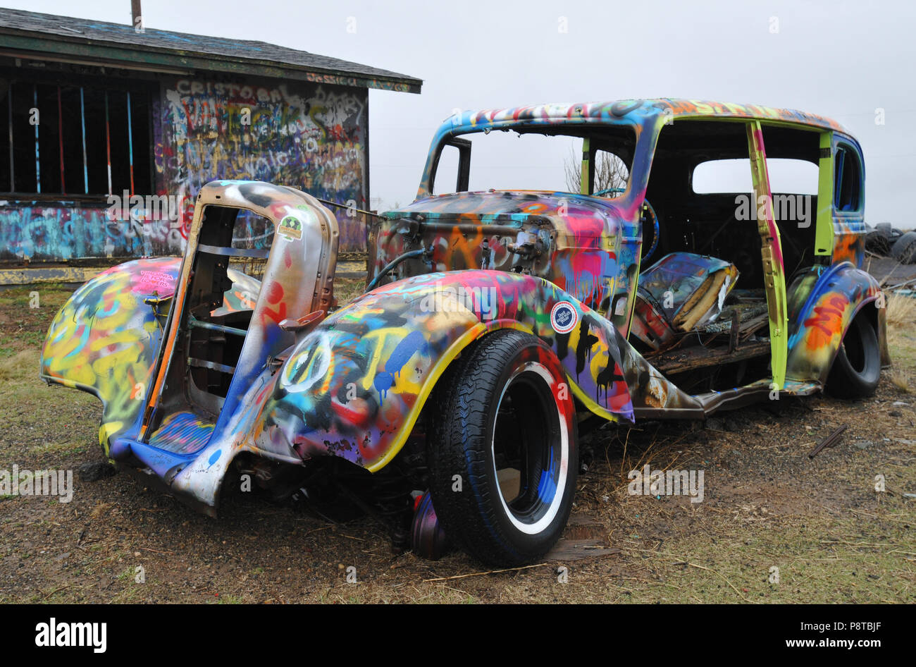 The shell of an old car sits covered in colorful spray-painted graffiti outside an abandoned trading post in the Route 66 town of Conway, Texas. Stock Photo