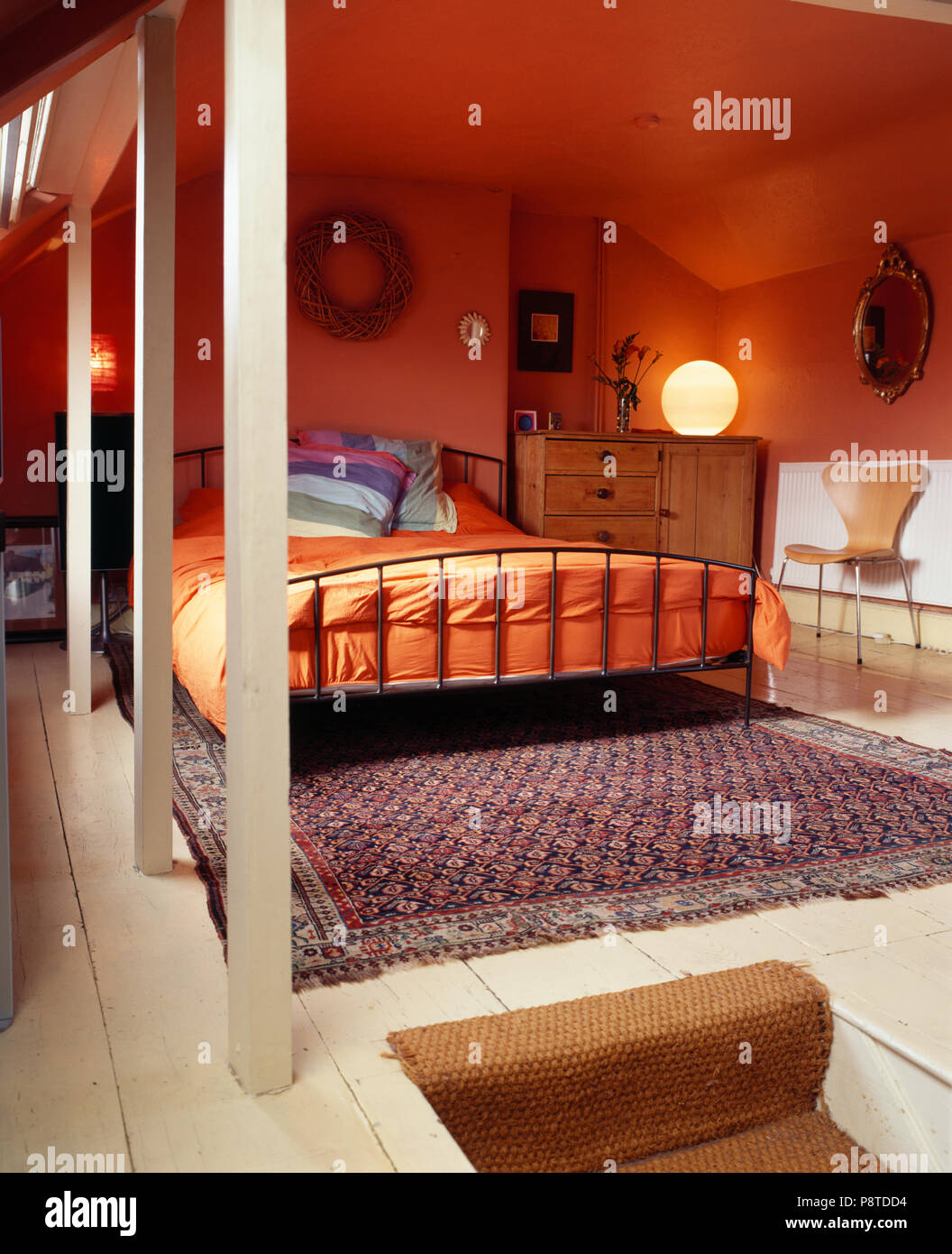 Orange duvet on metal bed in modern red loft conversion bedroom with antique oriental rug on floor Stock Photo