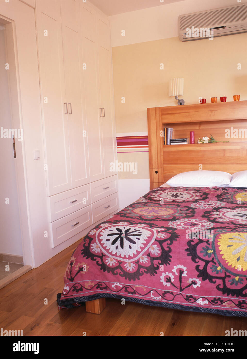 Air-conditioning on wall above fitted bed with patterned purple bedcover in coastal bedroom with fitted wardrobe Stock Photo