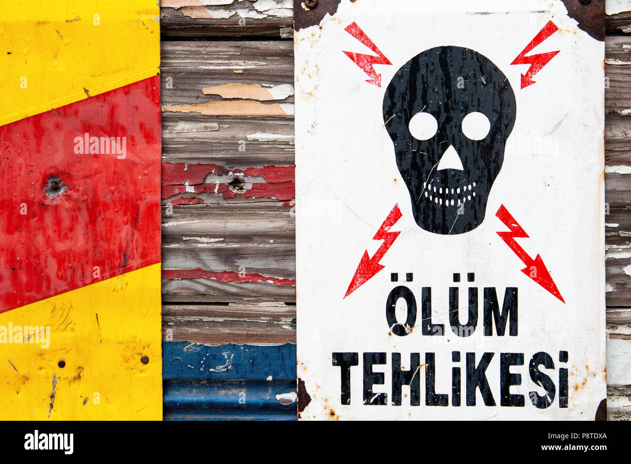 White metal danger of death warning sign in Turkish with a skull and lightning on wooden background. Stock Photo