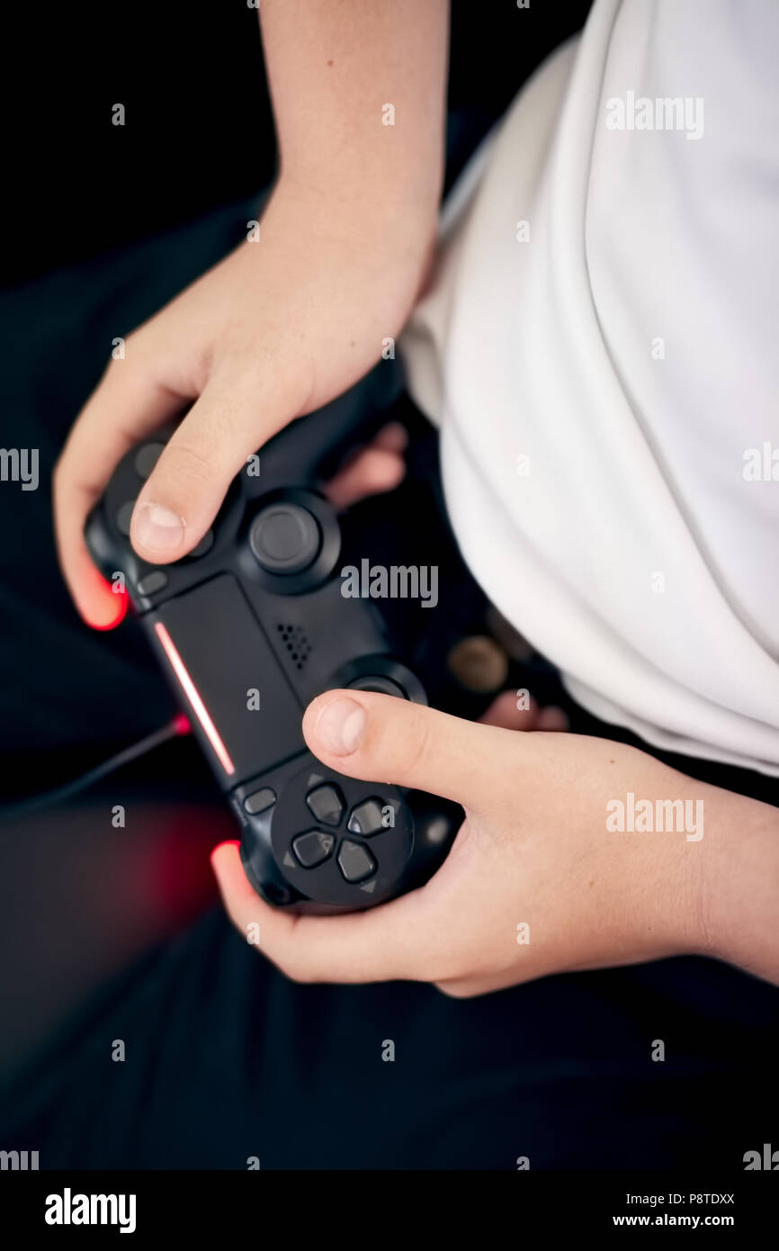 Hands of a Caucasian kid holding a black game pad and playing console game. Overhead view, close up. Stock Photo