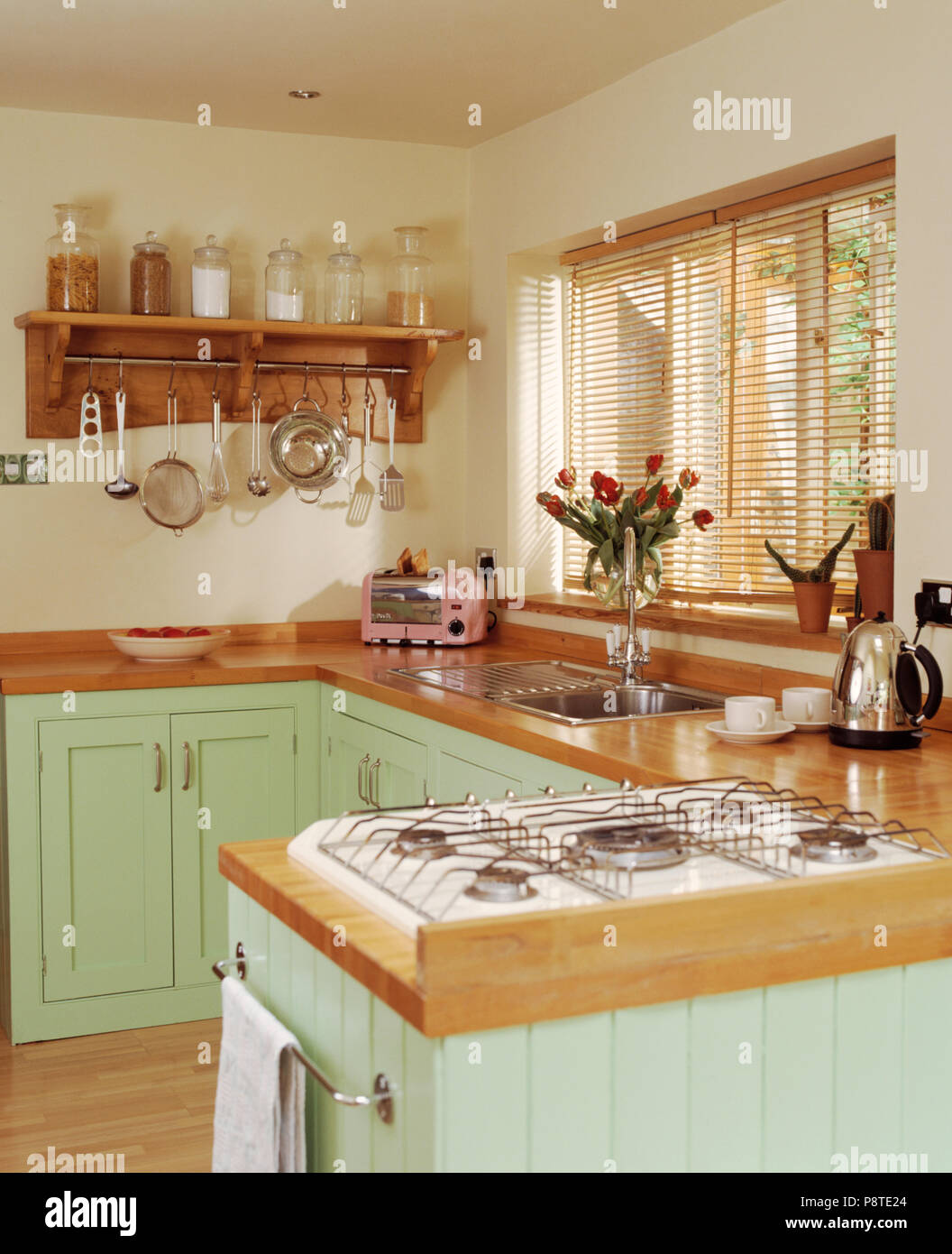 Gas hob in wooden worktop on peninsular unit in pastel green cottage